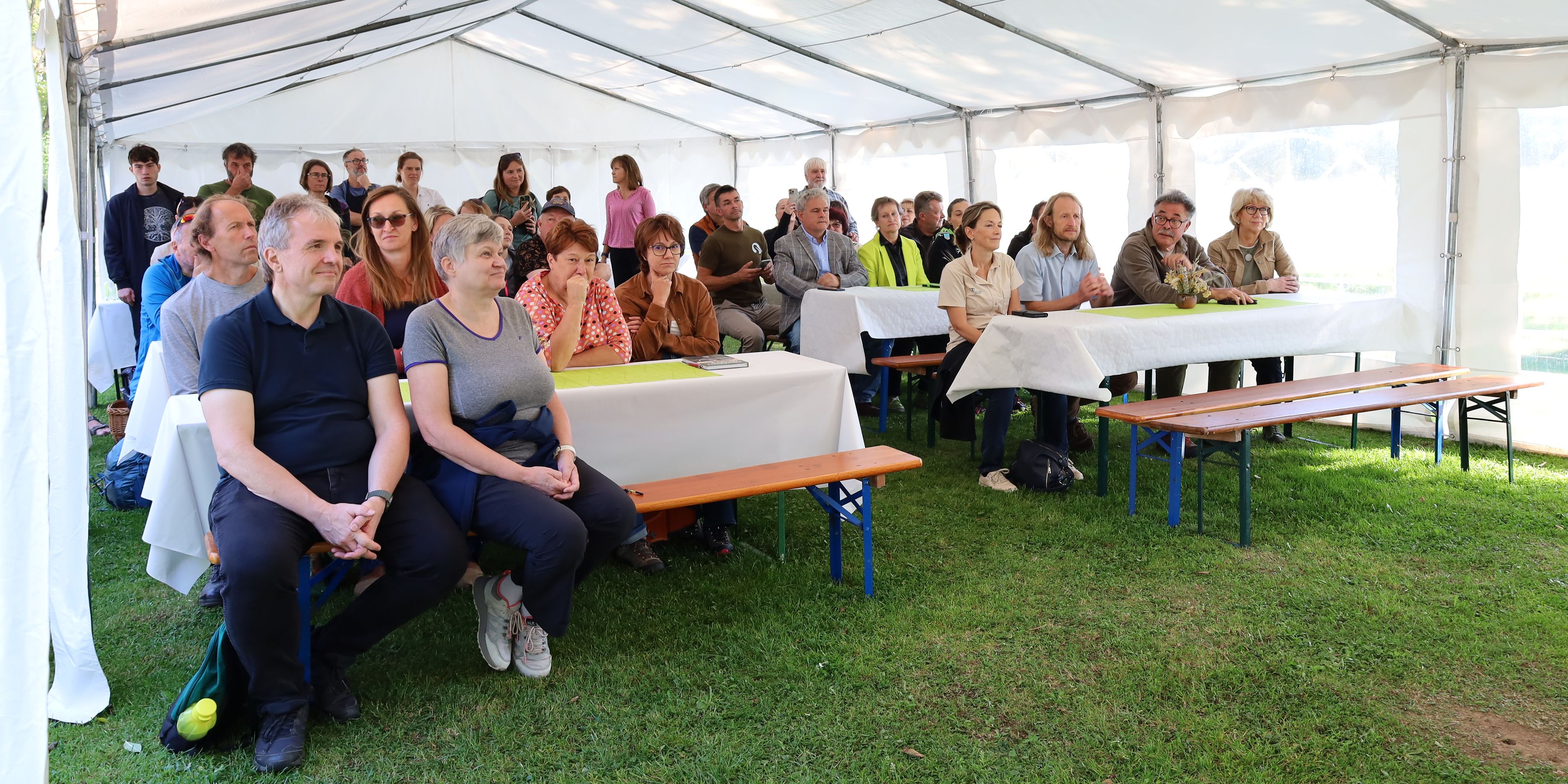 Lidé sedí ve stanu a poslouchají prezentaci knihy. 